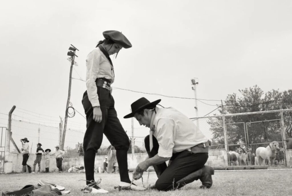 A man in a cowboy hat is tying the shoe of another man in a cowboy hat.