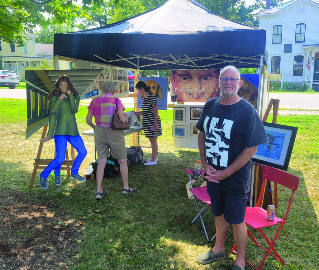 An artist stands in front of his booth at an art fair.