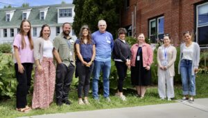 New school employees pose for a photograph on green grass outside a building.