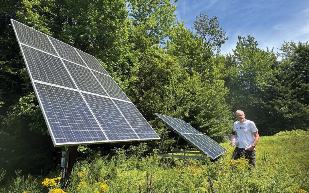 An author holds a copy of his book while standing next to a solar panel