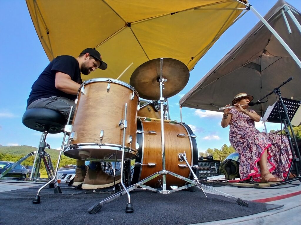 An experimental music band including a man on the drums and a woman on the flute plays outside