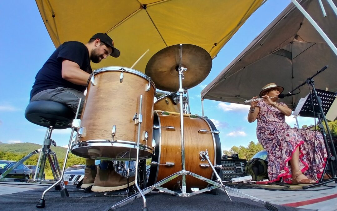 An experimental music band including a man on the drums and a woman on the flute plays outside