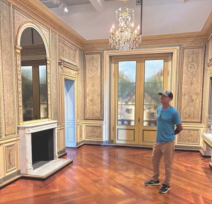 A man in a baseball cap stands in a restored Louis XVI-era room.