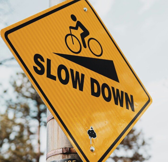 A diamond shaped yellow road side picturing a biker going downhill. It reads 'slow down'
